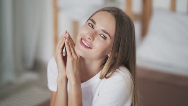 Porträt einer schönen jungen Frau, die auf dem Bett sitzt, in die Kamera blickt und lächelt — Stockvideo