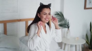 Sabahları beyaz bornozlu genç bir kadın yatakta dans ediyor, müzik dinliyor.