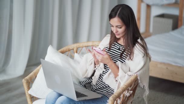 Žena na volné noze sedí v křesle používá notebook a smartphone pro práci doma — Stock video