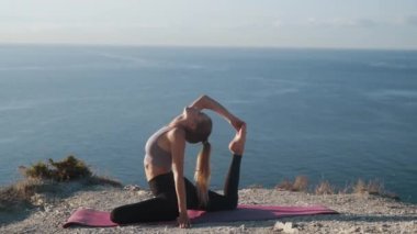 Dağın tepesinde yoga egzersizi yapan kadın, arka planda deniz, yavaş çekim