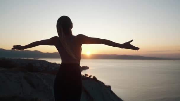 Sylwetka dziewczyny ćwiczy jogę, medytuje o wschodzie słońca z widokiem na morze, zwolnione tempo — Wideo stockowe
