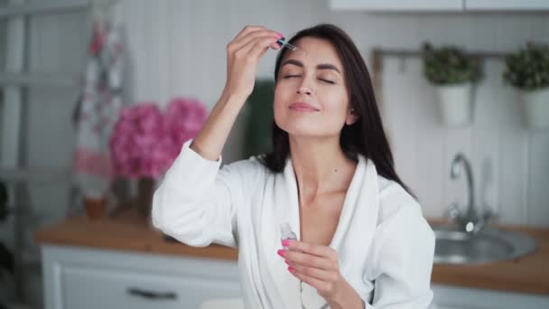 Retrato de mulher jovem aplica soro hidratante no rosto e faz massagem facial — Vídeo de Stock