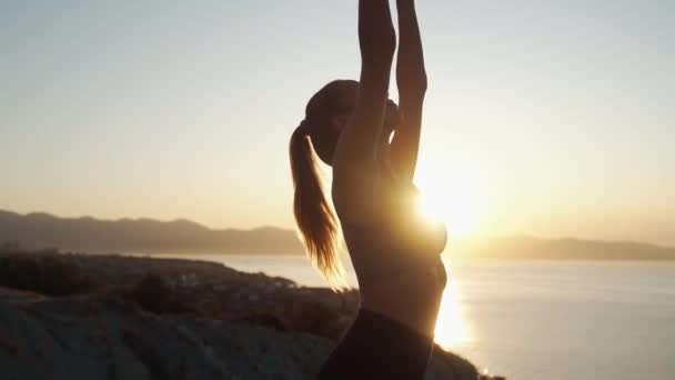 Silhueta de mulher pratica ioga no tapete e medita ao nascer do sol, câmera lenta — Vídeo de Stock