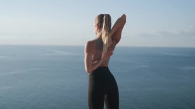 Kadın egzersizleri yapar ve deniz manzarası ile gün doğumunda uzanır, yavaş hareket