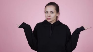 Kadın kollarını silker, jest yapar. Pembe arka planda soyutlanmış bir şekilde.