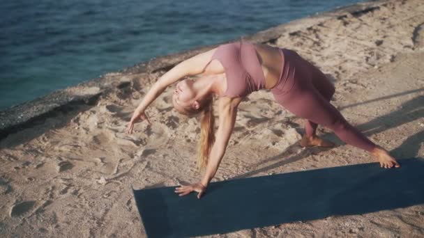 Kadın, okyanus manzaralı, yavaş çekimde, plajda yoga egzersizleri ve esneme hareketleri yapıyor. — Stok video