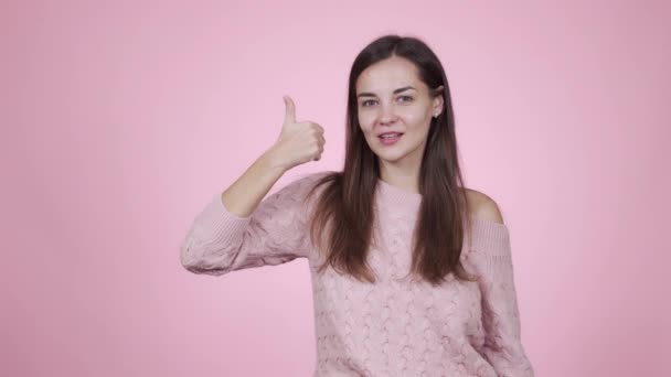 Mujer en jersey de punto muestra gesto pulgares hacia arriba aislado sobre fondo rosa — Vídeos de Stock