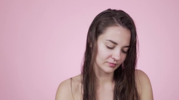 Portre kadını, pembe arka planda izole edilmiş duştan sonra ıslak saçlara yağ sürüyor. — Stok video