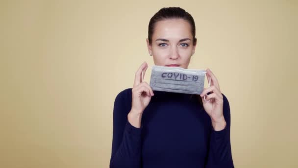 Портрет молодой женщины в защитной медицинской маске, смотрящей в камеру, изолированный — стоковое видео