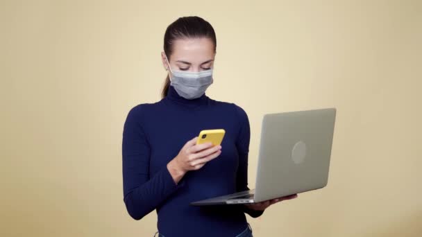 Kvinna i skyddande medicinsk mask använder laptop och smartphone för arbete, isolerade — Stockvideo