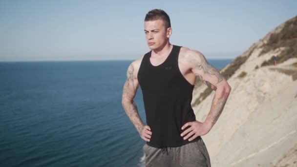 Deportista tatuado hace ejercicio al aire libre, hermosa vista al mar en el fondo — Vídeos de Stock