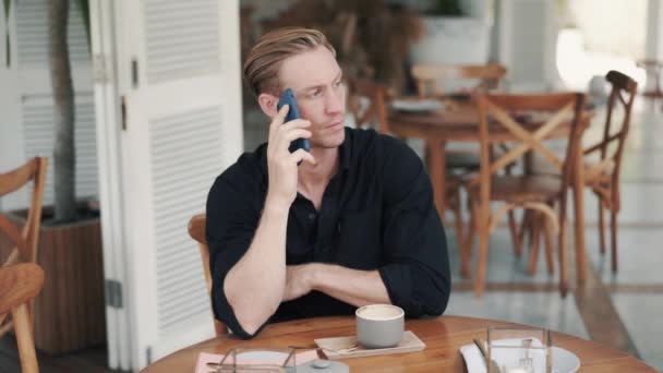 Retrato del hombre guapo tomando café en la cafetería moderna y hablando por teléfono — Vídeos de Stock