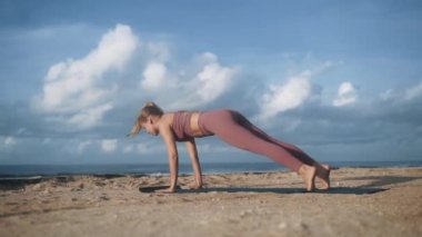 Okyanus sahilinde esneme ve yoga egzersizi yapan genç bir kadın.