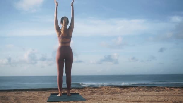Hátsó nézet nő csinál jóga gyakorlatok, nyújtózkodik a strandon, lassított felvétel — Stock videók