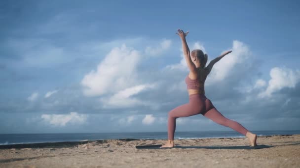 Vrouw doet yoga oefeningen, strekt zich uit op het strand met uitzicht op de oceaan, slow motion — Stockvideo