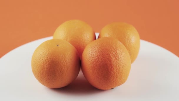 De cerca, cuatro naranjas sobre mesa giratoria blanca aisladas sobre fondo naranja — Vídeos de Stock