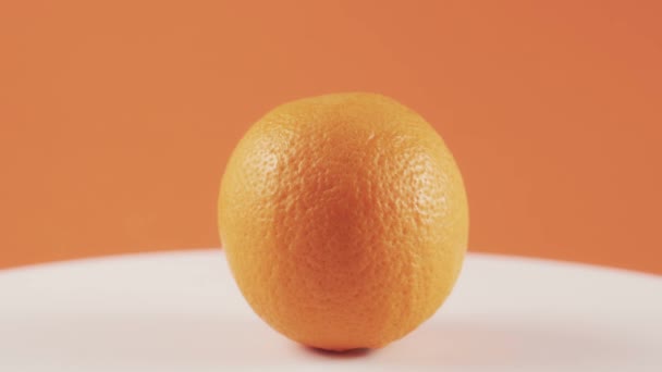 Gros plan, une orange sur la table tournante blanche isolée sur fond orange — Video