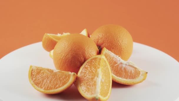 Primer plano, rodajas de naranja sobre mesa giratoria blanca aisladas sobre fondo naranja — Vídeos de Stock