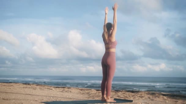 Жінка робить фізичні вправи на пляжі на сході сонця з видом на море, повільний рух — стокове відео