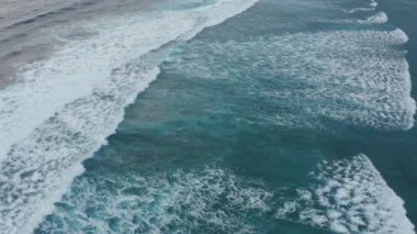 Mavi turkuvaz üzerinde güçlü dalgalar okyanusa çarpıyor ve köpürüyor..