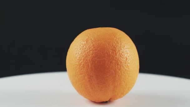 Primer plano de naranja sobre mesa giratoria blanca aislada sobre fondo negro — Vídeos de Stock