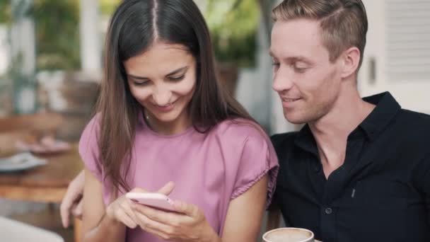 Ritratto di giovane uomo e donna nel caffè, usare lo smartphone, guardare lo schermo, parlare — Video Stock