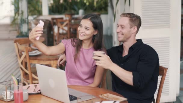 Blogueiros homem e mulher sentar no café ao ar livre, beber café, tirar selfie no telefone — Vídeo de Stock