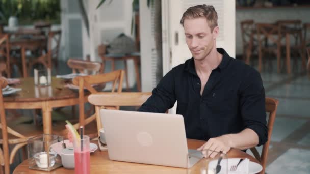 Hombre freelancer sentado en la mesa y la apertura de la computadora portátil para el trabajo en la cafetería moderna — Vídeos de Stock