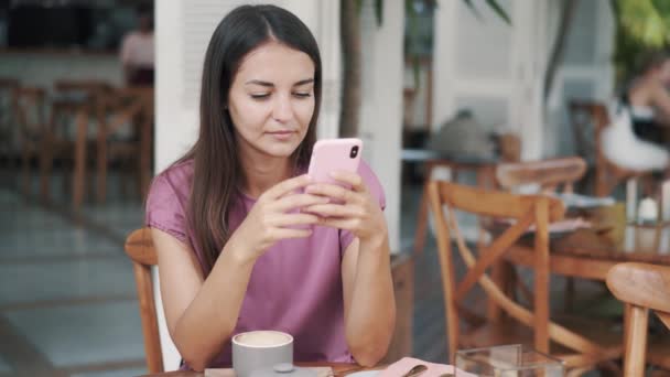 Retrato de hermosa chica sentada en la cafetería y el uso de teléfono móvil, envía un mensaje — Vídeos de Stock