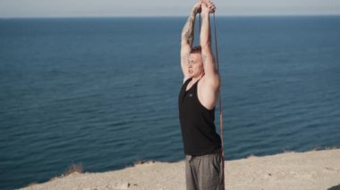 Siyah askılı kaslı sporcu açık havada lastik bantlarla trenler.