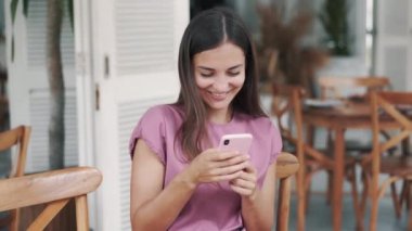 Kafede oturup cep telefonu kullanan mutlu bir kadının portresi.