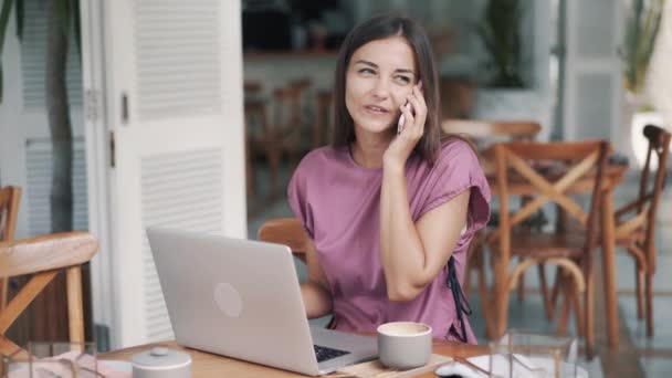 Mujer freelancer en la cafetería utiliza el ordenador portátil para el trabajo, hablando por teléfono, beber café — Vídeos de Stock