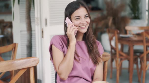 Portrét krásné brunetky žena mluví na telefonu ve stylové venkovní kavárně — Stock video