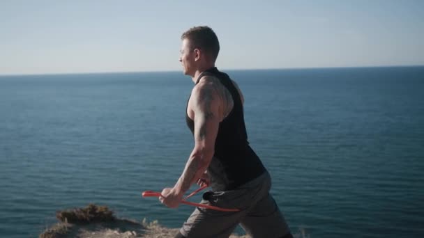 Svalnatý potetovaný sportovec trénuje paže a ramena s elastickými pásy venku — Stock video