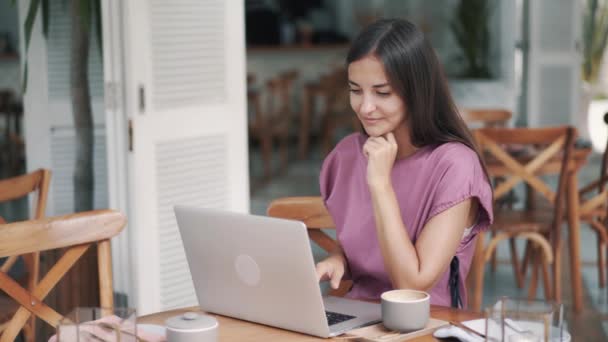 Retrato de una mujer freelancer sentada en la mesa y usando un portátil para trabajar en la cafetería — Vídeos de Stock