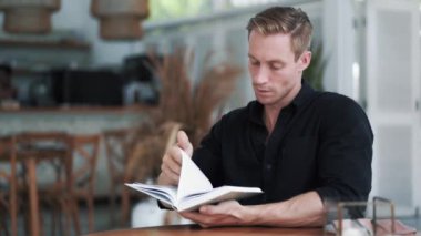Odaklanmış siyah gömlekli adam portresi modern açık hava kafesinde oturur ve kitap okur.