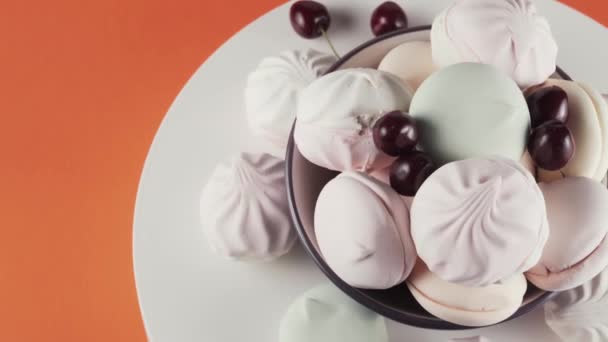 Coloured marshmallows and cherry at plate rotation over orange background. — Stock Video