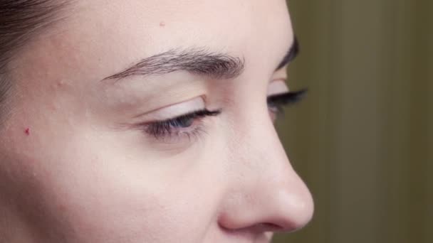 Närbild, sidovy av ung kvinna ansikte, ögat blinkar, beige bakgrund — Stockvideo