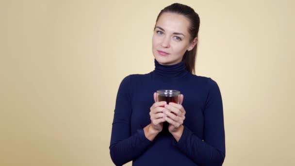 Portret van jonge lachende vrouw drinkt hete thee geïsoleerd op beige achtergrond — Stockvideo