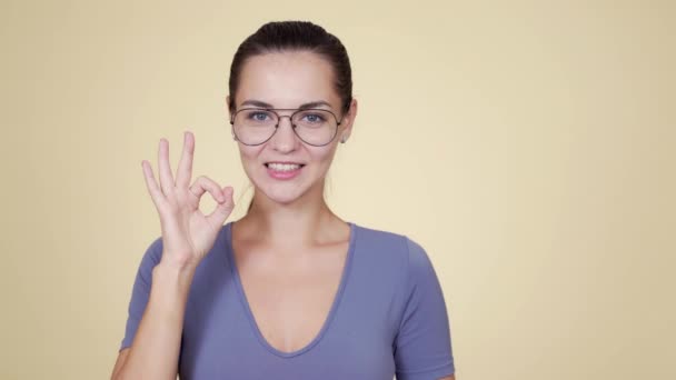 Retrato de mujer en gafas muestra ok o gran signo aislado sobre fondo beige — Vídeos de Stock