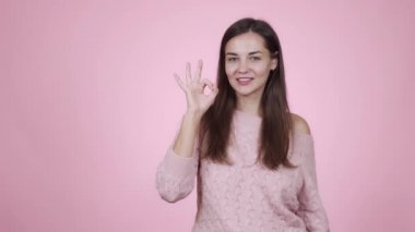 Örülmüş süveter giyen kız, pembe arka planda harika bir jest, harika bir işaret gösteriyor.