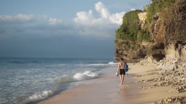 Surfista chico con tablas de surf camina a lo largo de la playa, olas suaves del océano lavado orilla — Vídeos de Stock