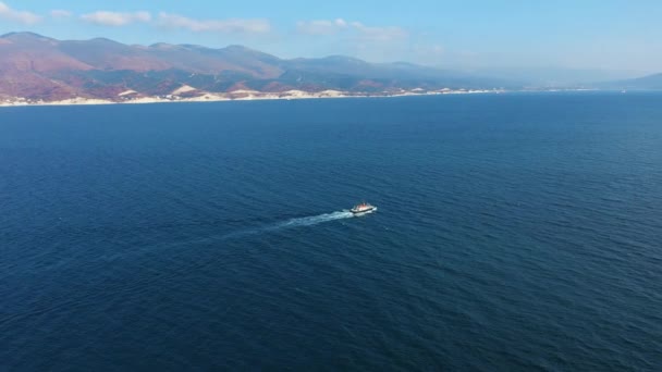 Вид с воздуха на небольшой корабль, плывущий вдоль морской бухты, горы на заднем плане — стоковое видео