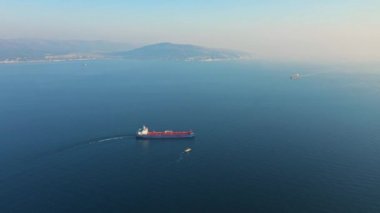Güneşli bir günde deniz limanından ayrılan büyük kargo gemisinin hava görüntüsü.