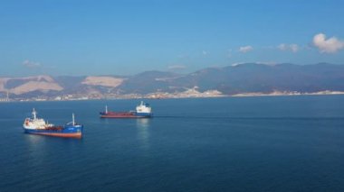Güneşli bir günde deniz limanından ayrılan iki büyük kargo gemisinin hava görüntüsü.