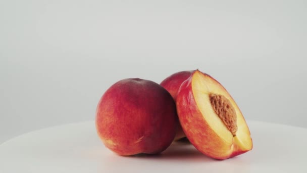 Close-up helft van nectarine en twee perziken op roterende tafel op witte achtergrond — Stockvideo