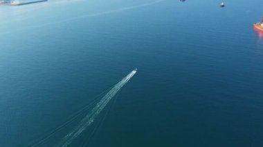 Deniz körfezi boyunca giden küçük geminin havadan görünüşü, arka planda dağlar.