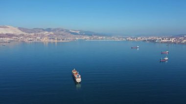 Güneşli bir günde deniz limanından ayrılan büyük kargo gemisinin hava görüntüsü.