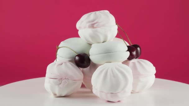 Färgade marshmallows och körsbär på plattan rotation över rosa bakgrund. — Stockvideo