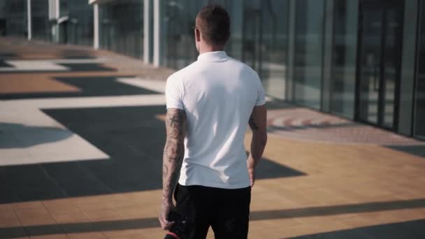도시 공간을 거닐고 있는 날씬하고 자신있는 남성 사진사의 뒷모습 — 비디오